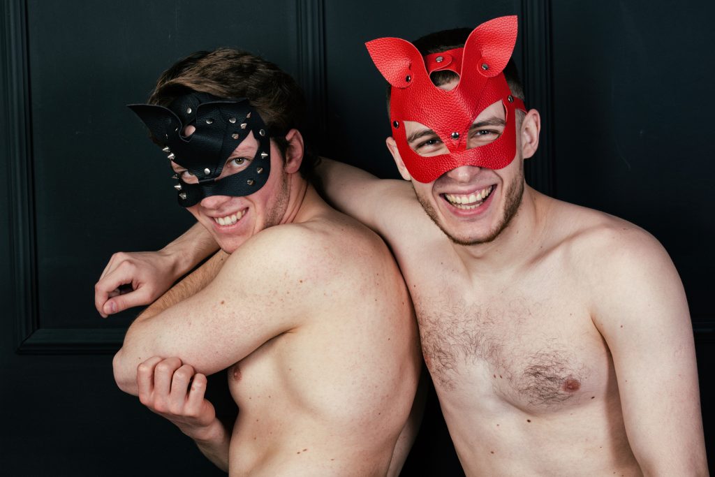 Two smiling shirtless men wearing leather masks